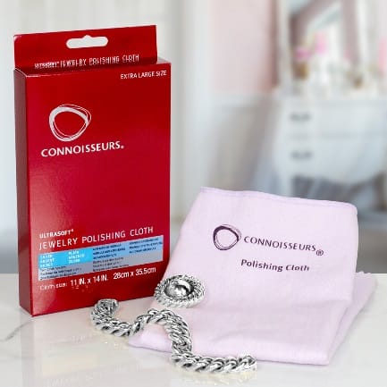 A pink towel with a CONNOISSEURS SILVER JEWELLERY POLISHING CLOTH and a necklace next to it.
