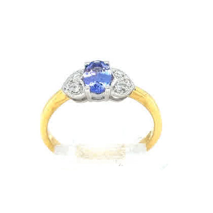 The Tanzanite and Diamond Cluster Dress Ring in 18ct Yellow Gold features a central blue tanzanite gemstone with two small diamonds, presented on a clear stand against a white background.