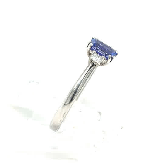 The Tanzanite and Diamond Trilogy Dress Ring in 9ct white gold features a rectangular blue tanzanite center flanked by two diamonds, displayed from a side angle.