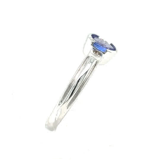 The Tanzanite Trilogy Dress Ring in 9ct white gold features a round blue gemstone in a prong setting, shown from the side against a white background.