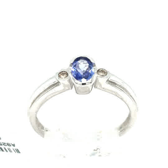 The Tanzanite Trilogy Dress Ring in 9ct white gold features an oval-cut blue tanzanite center stone flanked by two round accent stones in a classic trilogy design.