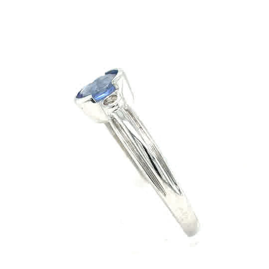 The Tanzanite Trilogy Dress Ring in 9ct white gold features a round blue tanzanite gemstone in a bezel setting, shown from the side against a white background.