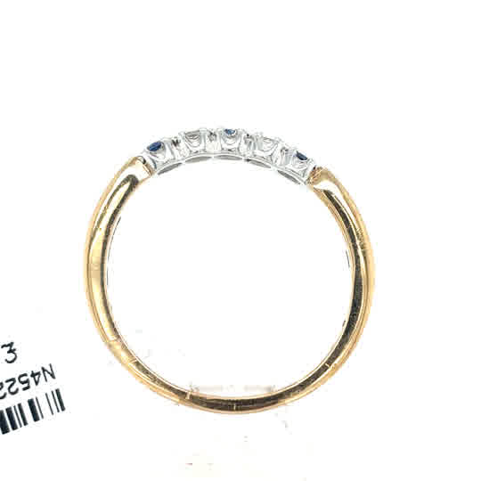 The Cym Welsh Gold Diamond and Sapphire Half Eternity Ring is shown from a side angle, displaying five clear stones in a white metal setting atop gold, with a partially visible barcode.