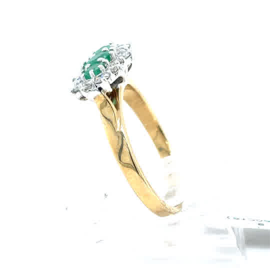 The Emerald and Diamond Cluster Boat Dress Ring in 9ct yellow gold showcases a vivid green emerald at its center, accented by sparkling diamonds in a classic cluster setting, displayed on a white background.