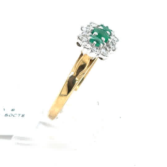 The Emerald and Diamond Cluster Boat Dress Ring in 9ct yellow gold features a central green oval emerald framed by a sparkling halo of diamonds.