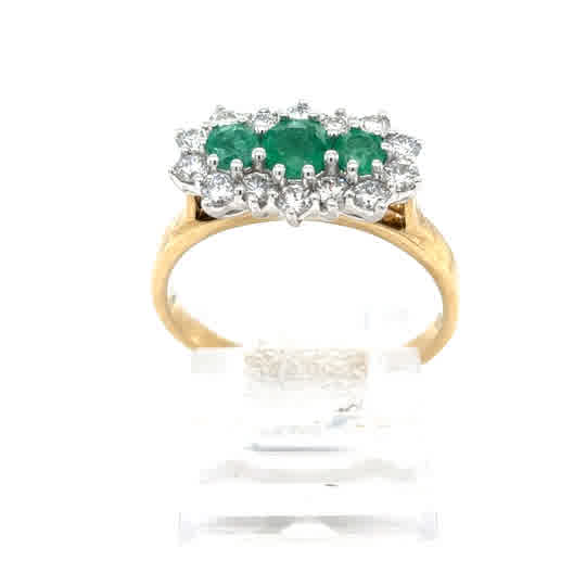 The Emerald and Diamond Cluster Boat Dress Ring in 9ct yellow gold features three oval green stones at the center, surrounded by a halo of small clear stones, and is displayed on a clear stand against a white background.