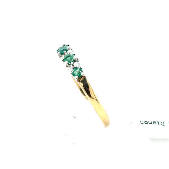 The Emerald and Diamond Half Eternity Ring in 9ct yellow gold features alternating small green emeralds and clear diamonds set in a curved row along the band.