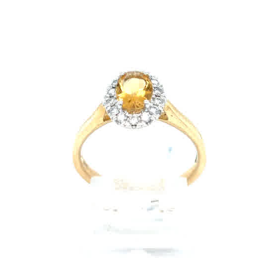 The Citrine & Diamond Halo Dress Ring in 9ct yellow gold features a vibrant oval citrine gemstone at the center, surrounded by sparkling diamonds in a halo setting and elegantly displayed on a stand.