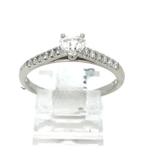 The Platinum Heart Diamond Engagement Ring features a heart-shaped diamond center with smaller stones along the band, elegantly displayed on a clear stand.