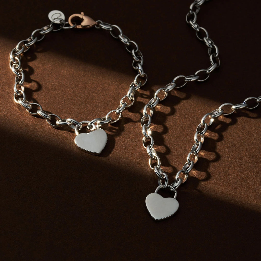 The Clogau Cariad® Sterling Silver Padlock Bracelet, featuring a heart padlock pendant, is displayed on a brown surface under partial lighting.