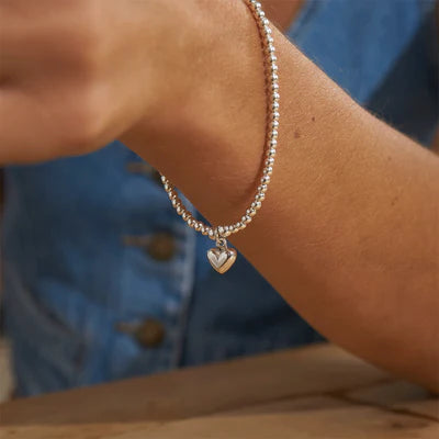 Someone wears the ChloBo Cute Charm Puffed Heart Bracelet with a blue denim top that has visible buttons.
