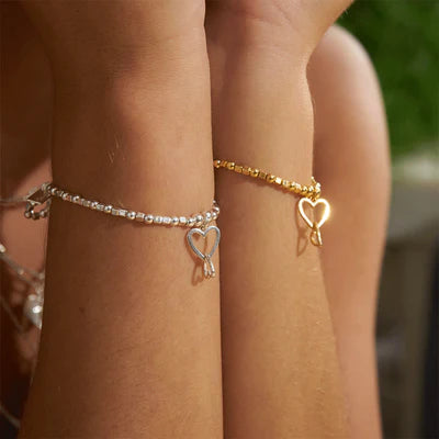 Two arms wear ChloBo Mini Cube Interlocking Love Heart Bracelets in silver and gold, each with a heart charm—a perfect gift for her.