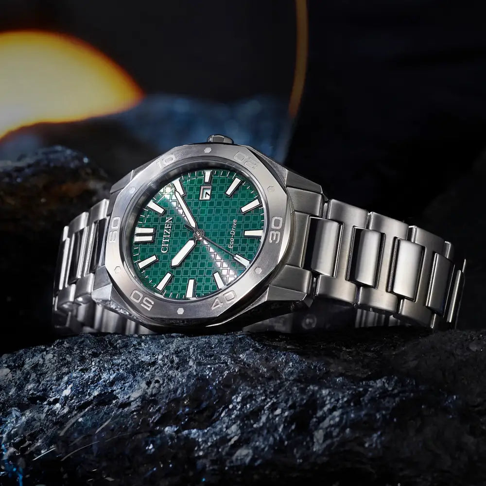The Citizen Men's Steel Green Dial Bracelet Watch BM7630-80X, featuring a green textured dial and silver indices, rests on a rocky surface.