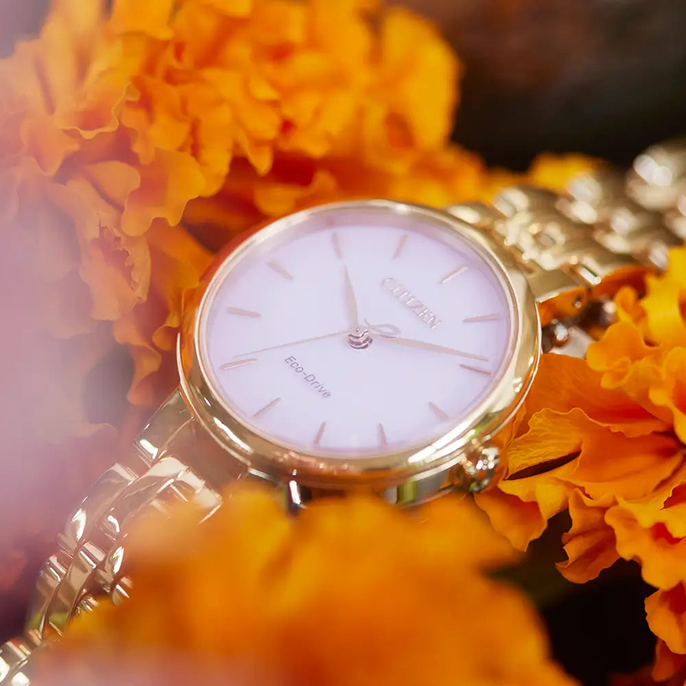 A Citizen Ladies Silhouette Pink Dial Gold Tone Watch (EM0993-82X) is elegantly encircled by vibrant orange marigold flowers.