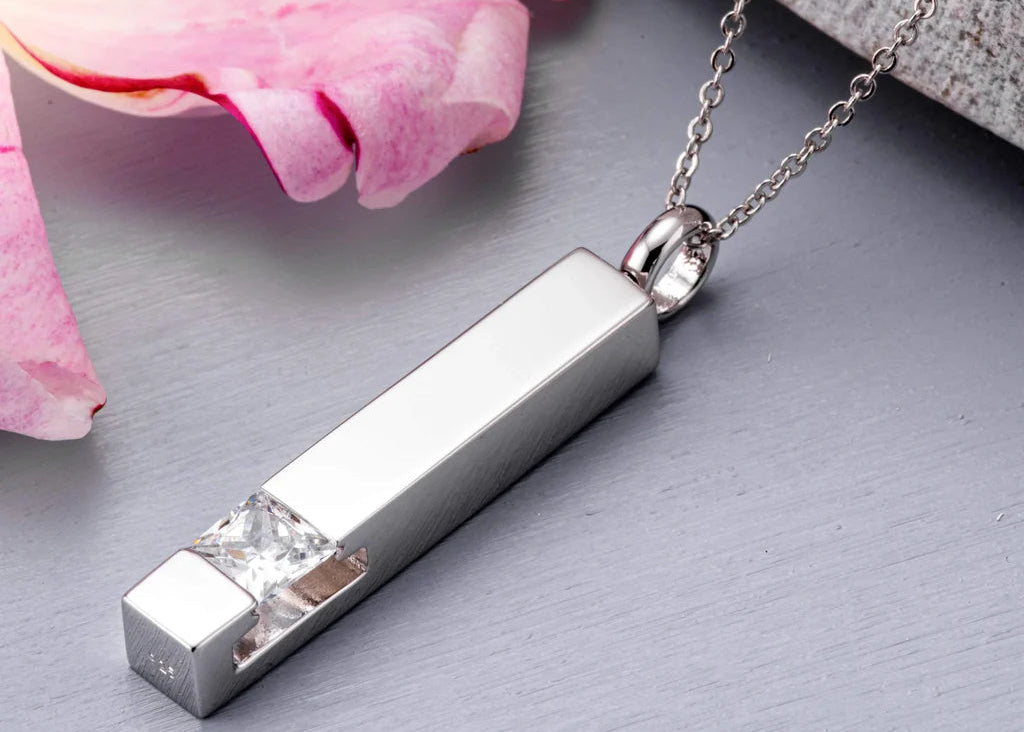 Silver pendant necklace with a diamond on a gray surface with pink flowers.