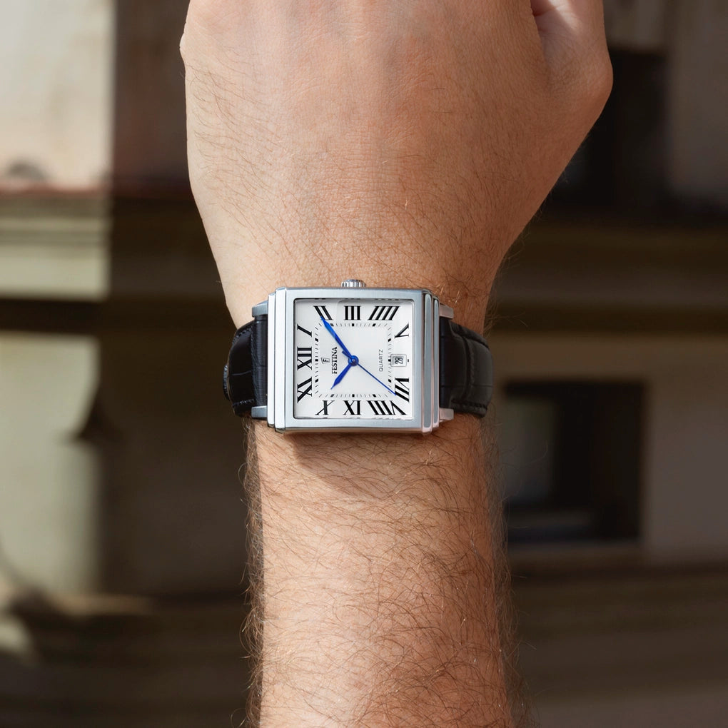 A wrist wearing the Festina Men's Silver Dial Watch (F20681/1) featuring a square stainless steel case, Roman numerals, silver dial, blue hands, and a black leather strap.