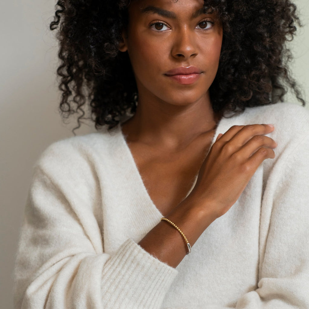 A woman with curly hair wearing a white sweater is also wearing the TI SENTO – BANGLE 2944SY.