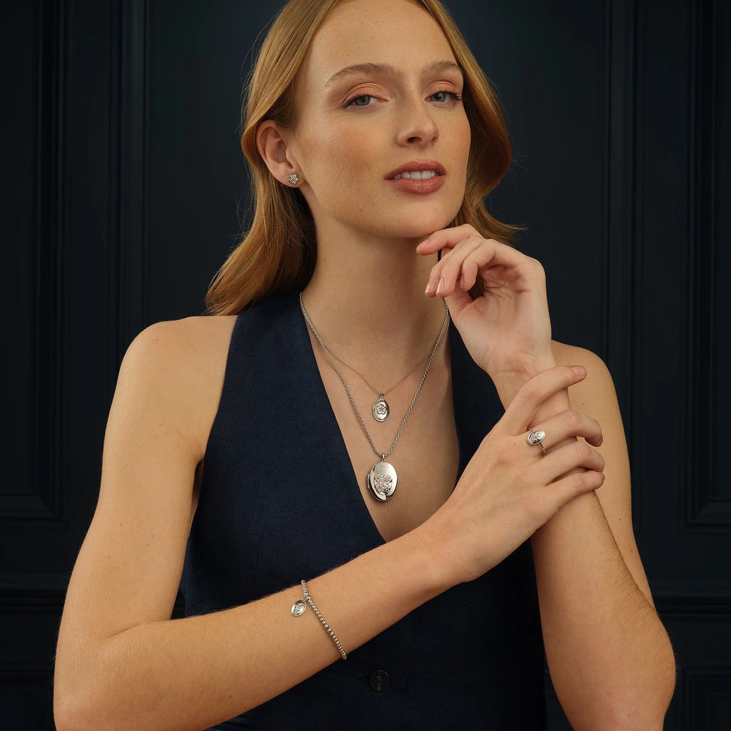 A woman is posing with the Clogau Forget Me Not Locket 3SFMN0618 and bracelet.