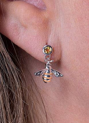 A woman's ear with a Clogau Honey Bee Drop Earrings 3SHNBDE dangling from it.