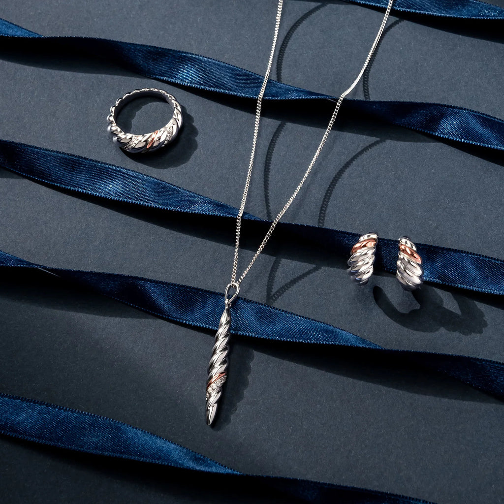 A Clogau Lover’s Twist Earrings 3SLTW0614 necklace, ring, and earrings on a blue background.