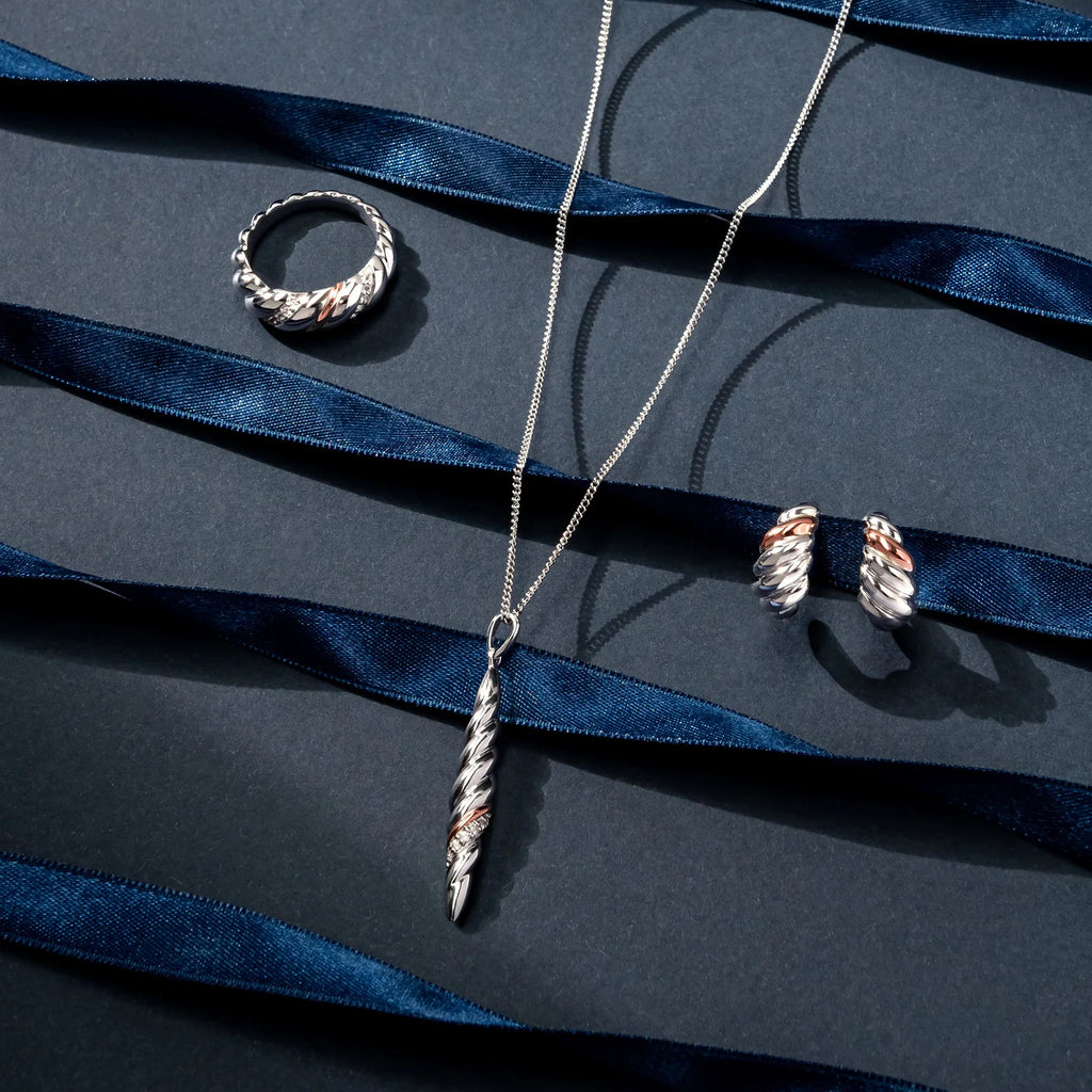 A silver necklace, Clogau Lover's Twist Ring 3SLTW0615, and earrings on a blue background.