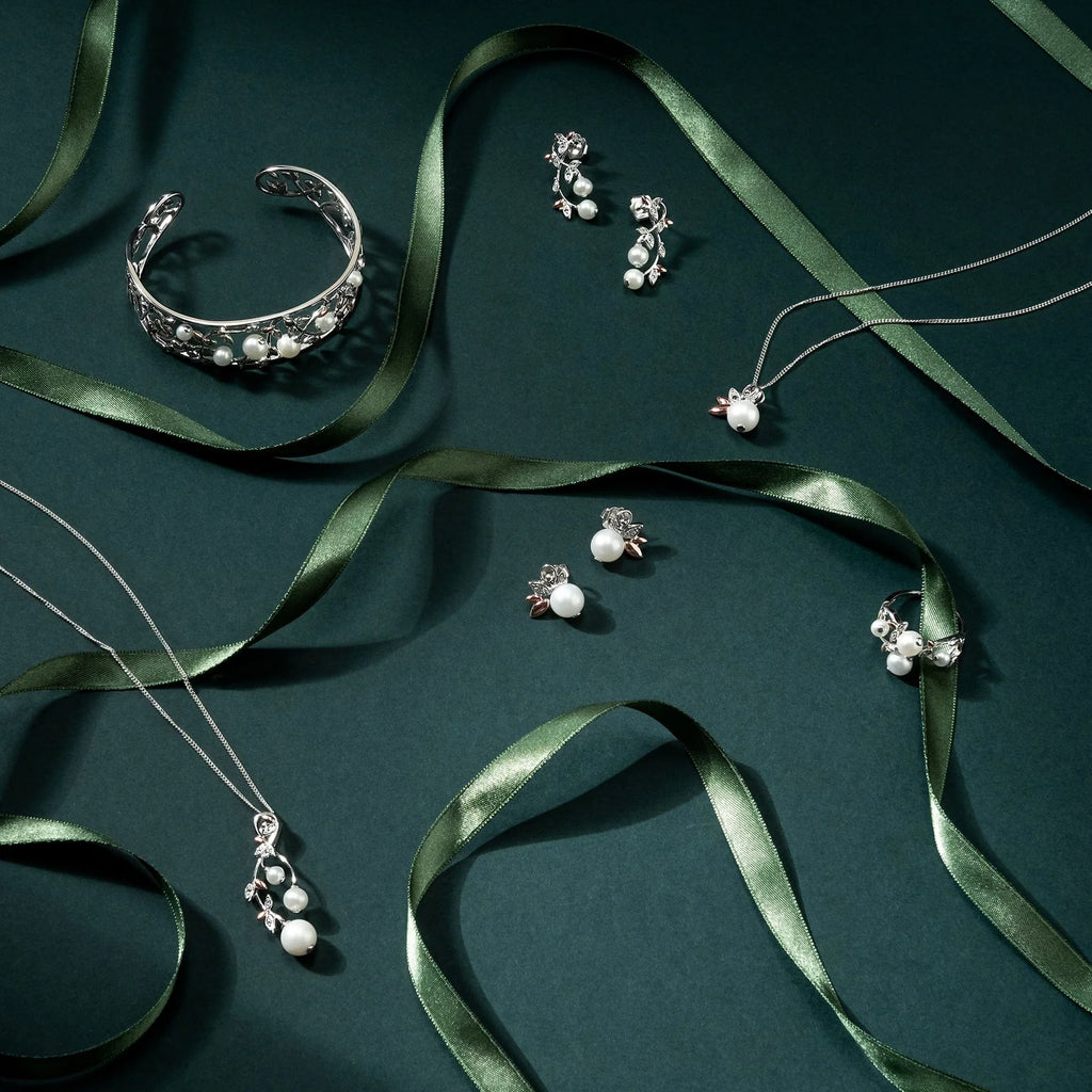 A collection of Clogau Lily of the Valley Pendant 3SLYV0600 and silver jewelry on a green background.