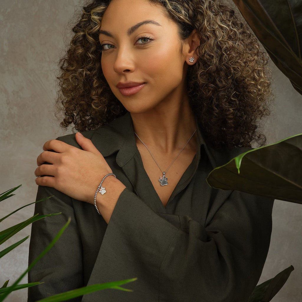 A woman with curly hair posing in front of Clogau Paw Print Stud Earrings 3SPWP0616.
