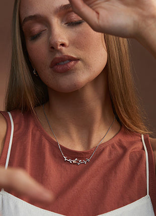 A woman wearing a NEW Clogau Vine of Life White Topaz Necklace 3STOL0237 with a heart on it.