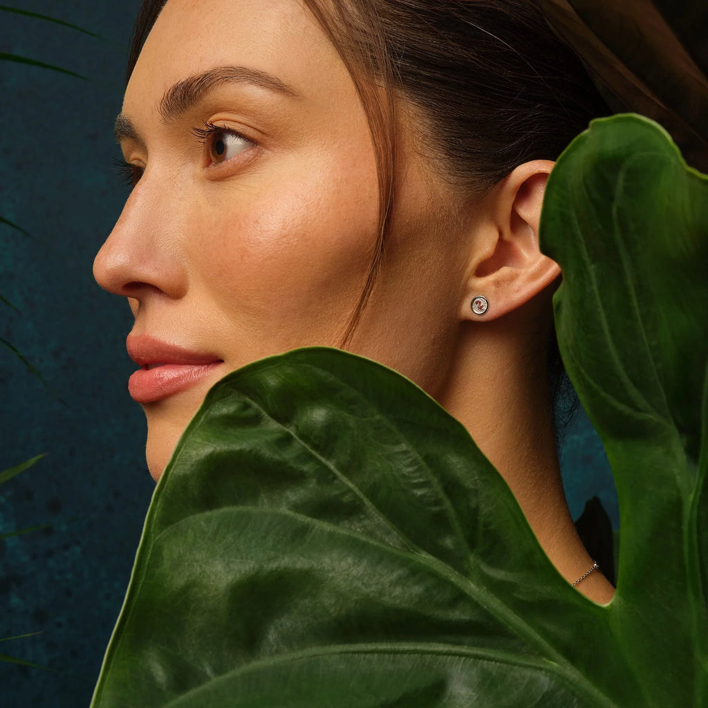 A woman wearing Clogau Tree of Life Insignia Stud Earrings 3STOL0604 in front of a green leaf.