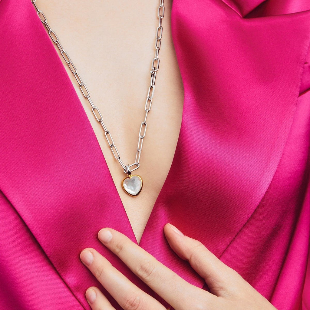 A woman in a pink suit is holding a TI SENTO – Milano Mother of Pearl Colour Pendant with a heart on it.
