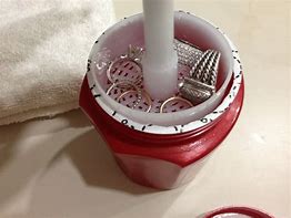A red CONNOISSEURS SILVER JEWELLERY CLEANER filled with jewelry and a toothbrush.