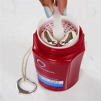 A person is holding a red container of CONNOISSEURS SILVER JEWELLERY CLEANER with a silver chain.