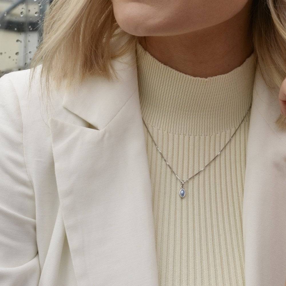 A woman wearing a white jacket and a Birthstone Necklace December- Blue Topaz.