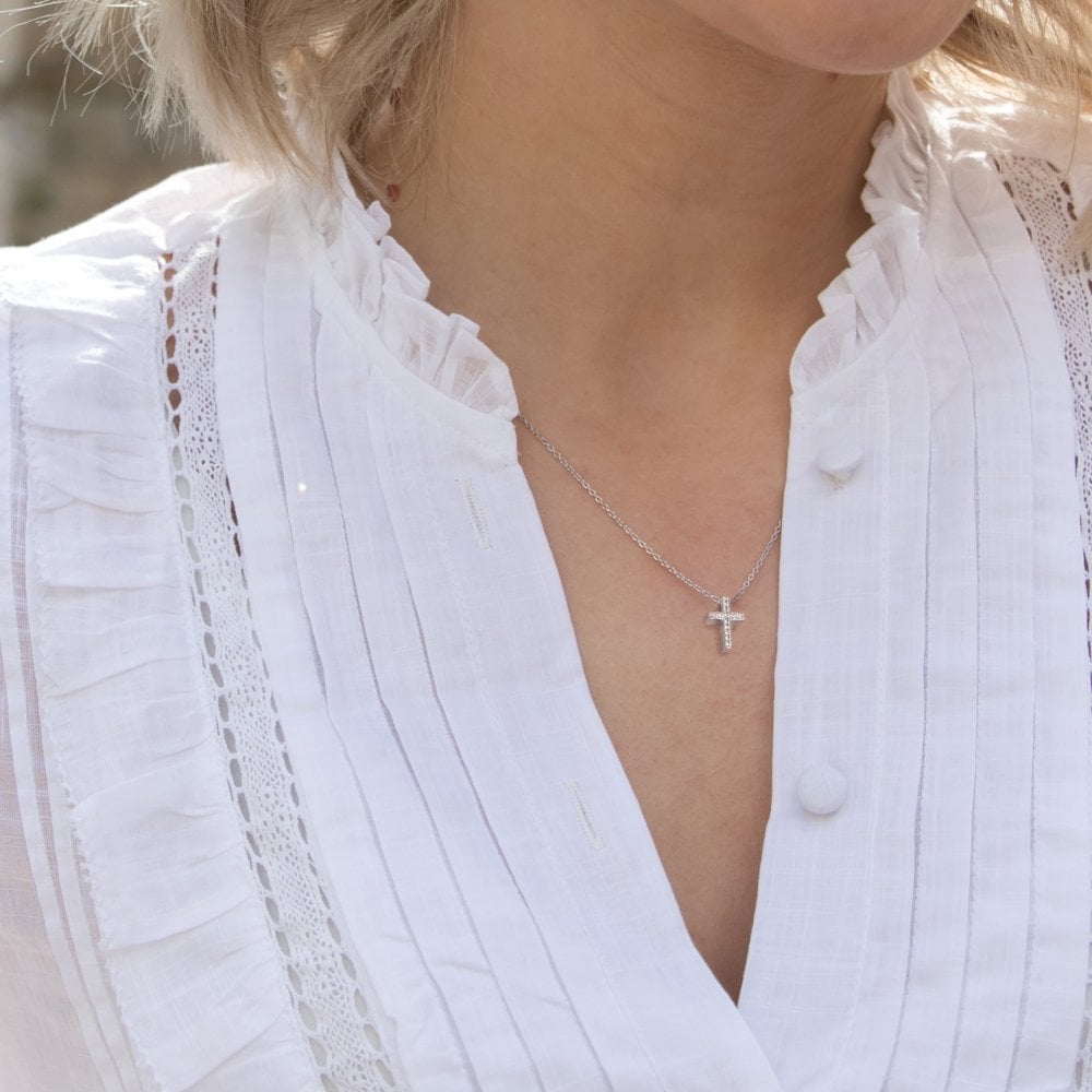 A woman wearing a white shirt with a HOT DIAMONDS Striking Cross Pendant - DP696.